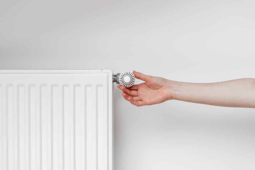 Main ajustant un thermostat blanc sur un radiateur moderne, contrôlant la température et l'économie d'énergie.