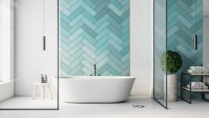 Salle de bain moderne avec baignoire blanche, mur carrelé turquoise à chevrons. Cloisons en verre, plante et serviettes.