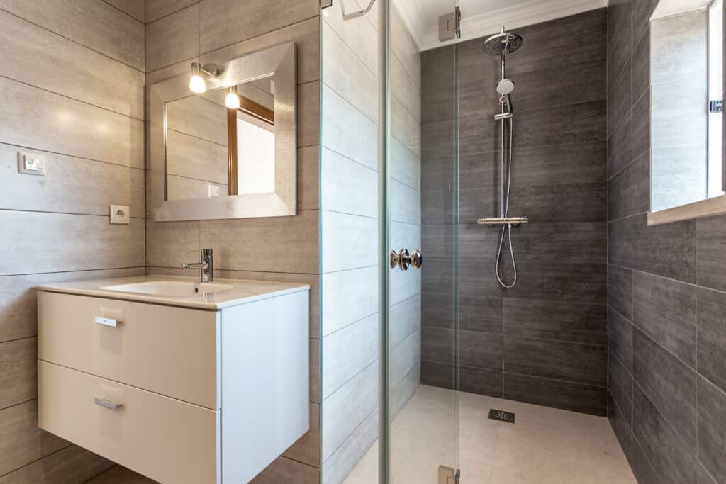 Salle de bain moderne avec meuble vasque blanc, miroir argenté texturé et douche à l'italienne carrelée gris foncé.
